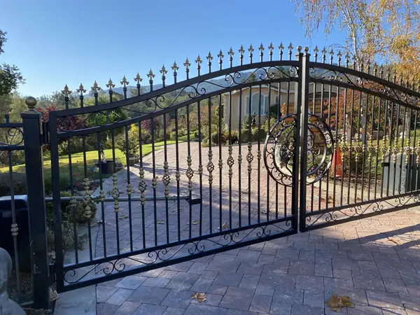 Arched wrought iron gate across a paver driveway