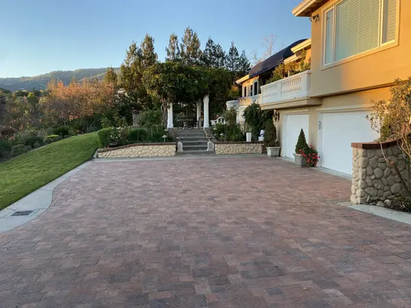 Red-toned paver driveway leading to a hillside home