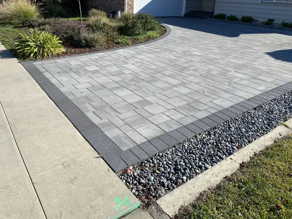 Gray paver driveway with a charcoal border and river rock edge
